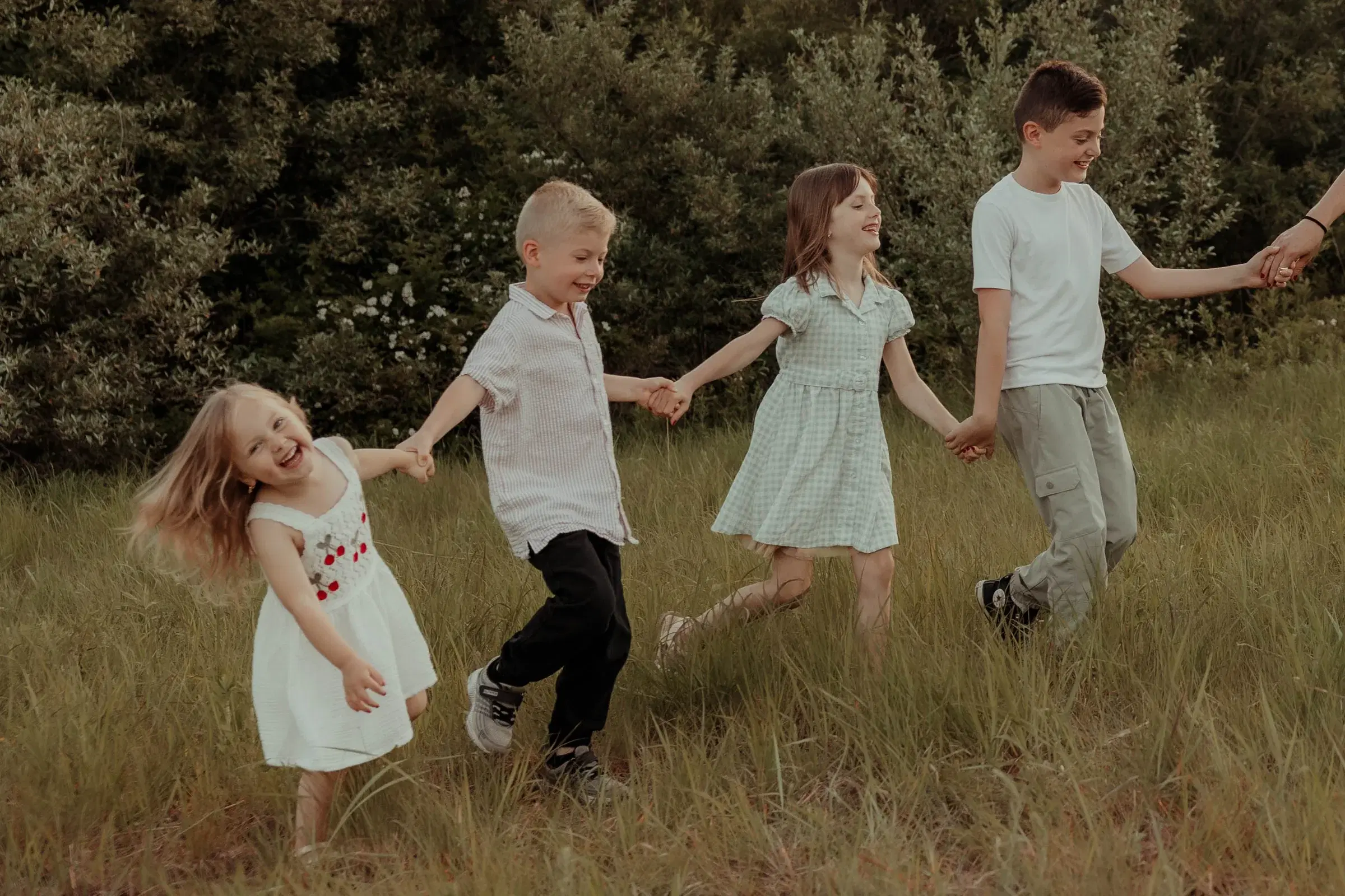 Lauren and Chase Reidinger's four children holding hands in a grassy field